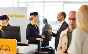 A passenger is communicating with a Lufthansa crew member at the gate, whilst holding his mobile device.