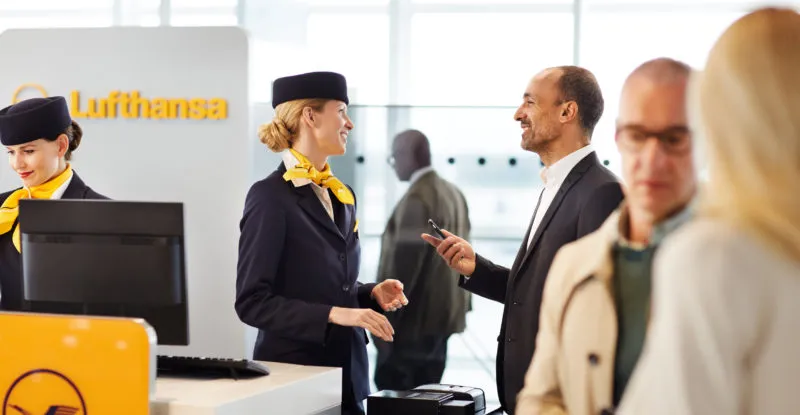 A passenger is communicating with a Lufthansa crew member at the gate, whilst holding his mobile device.