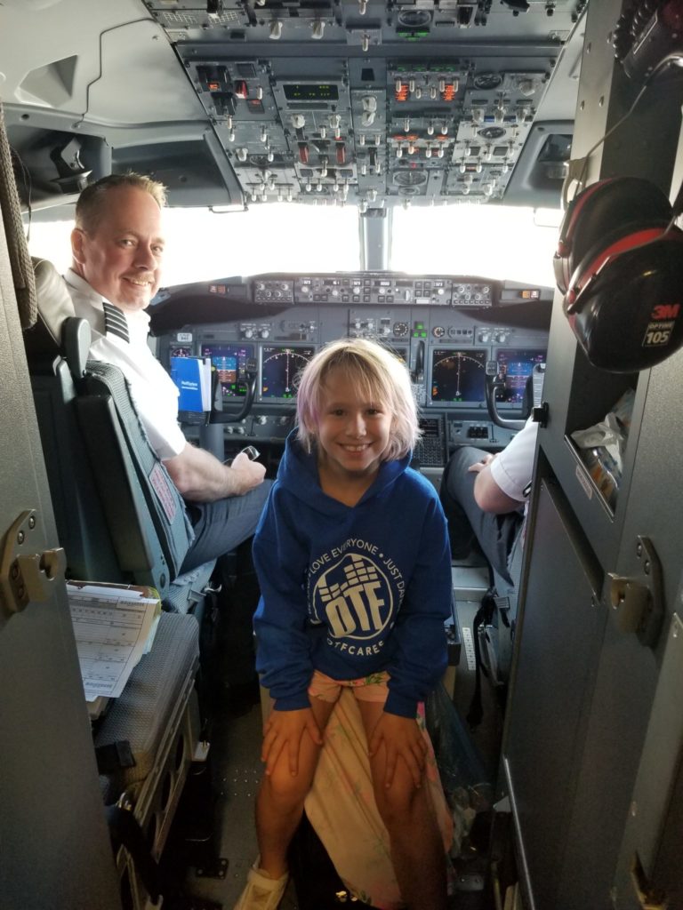 A young girl is sitting in the cockpit of a swoop aircraft posing for a picture with the pilots. 