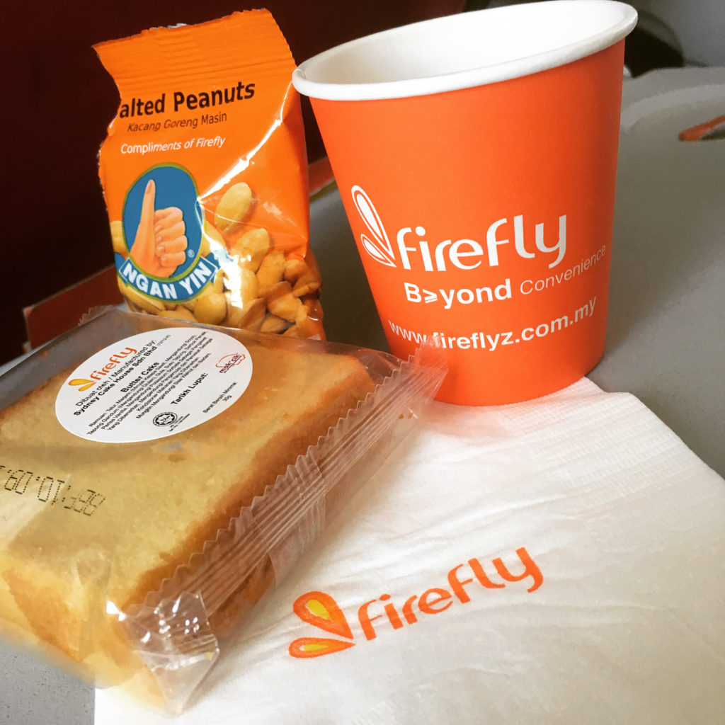 pound cake, firefly cuo and bag of salted peanuts on the tray table of an aircraft seat