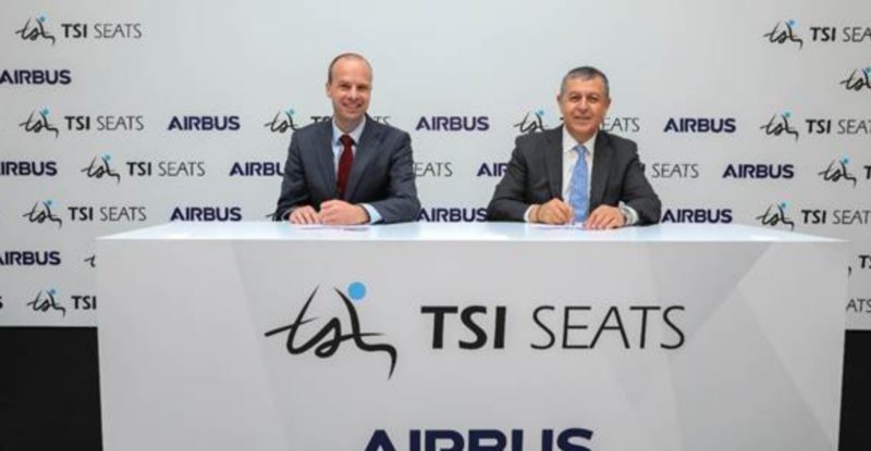 two men sitting at a table with a tsi and airbus logo on it