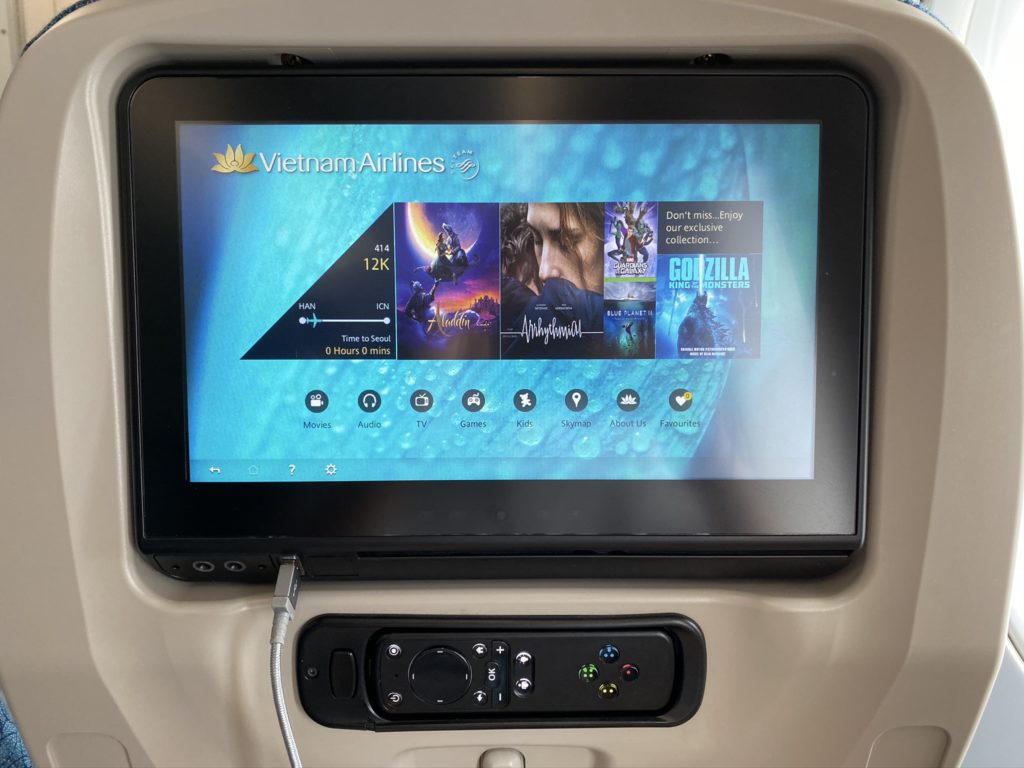 Panasonic IFE screen showing movie selection and remote in seatback of aircraft seat