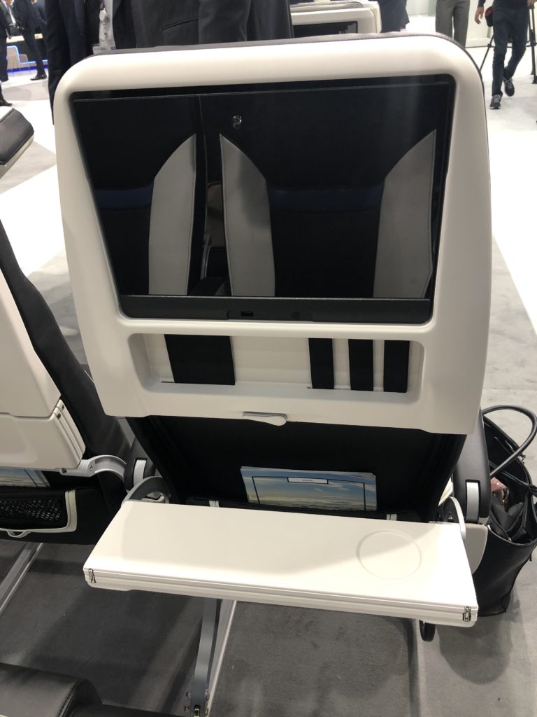 The new Z400 economy class seat headrest showing embedded seatback IFE, seatback straps for glasses and other personal devices and a bi-fold tray table and 