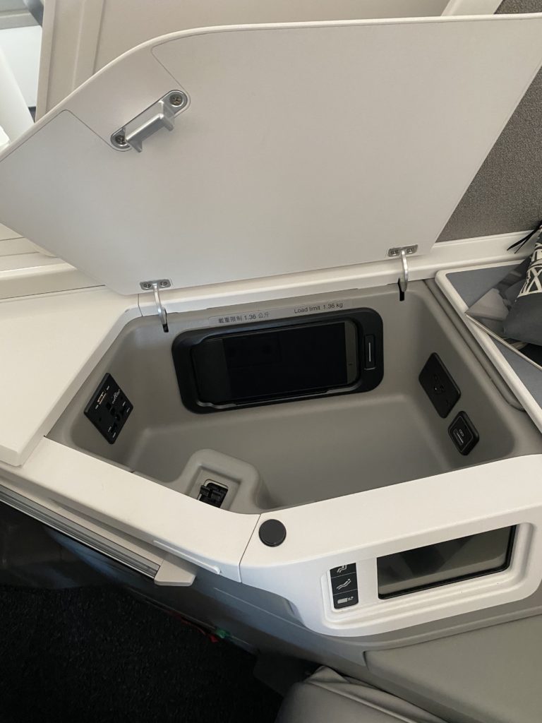 A cubby in the new business class seat containing a remote control and power outlets