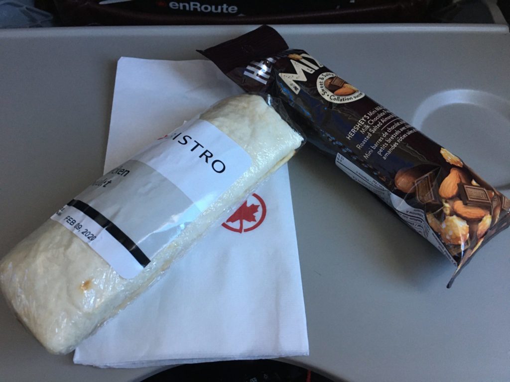 Bistro chicken wrap and Herseys snack mix displayed atop of an Air Canada napkin on tray table