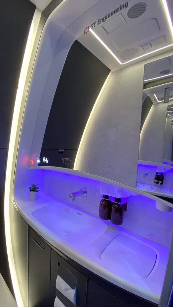 The sink deck slopes upwards and forms part of the sidewall. This image shows the slope, a cured mirror and purple LED lighting around the faucet fixtures