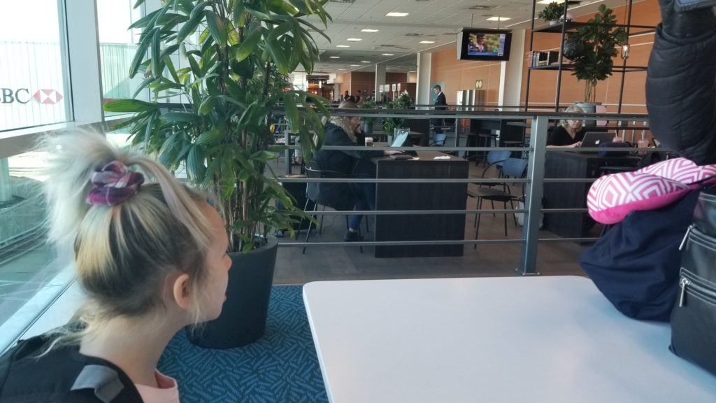 A few people scattered withing different airport seating options with laptops open many empty seats around