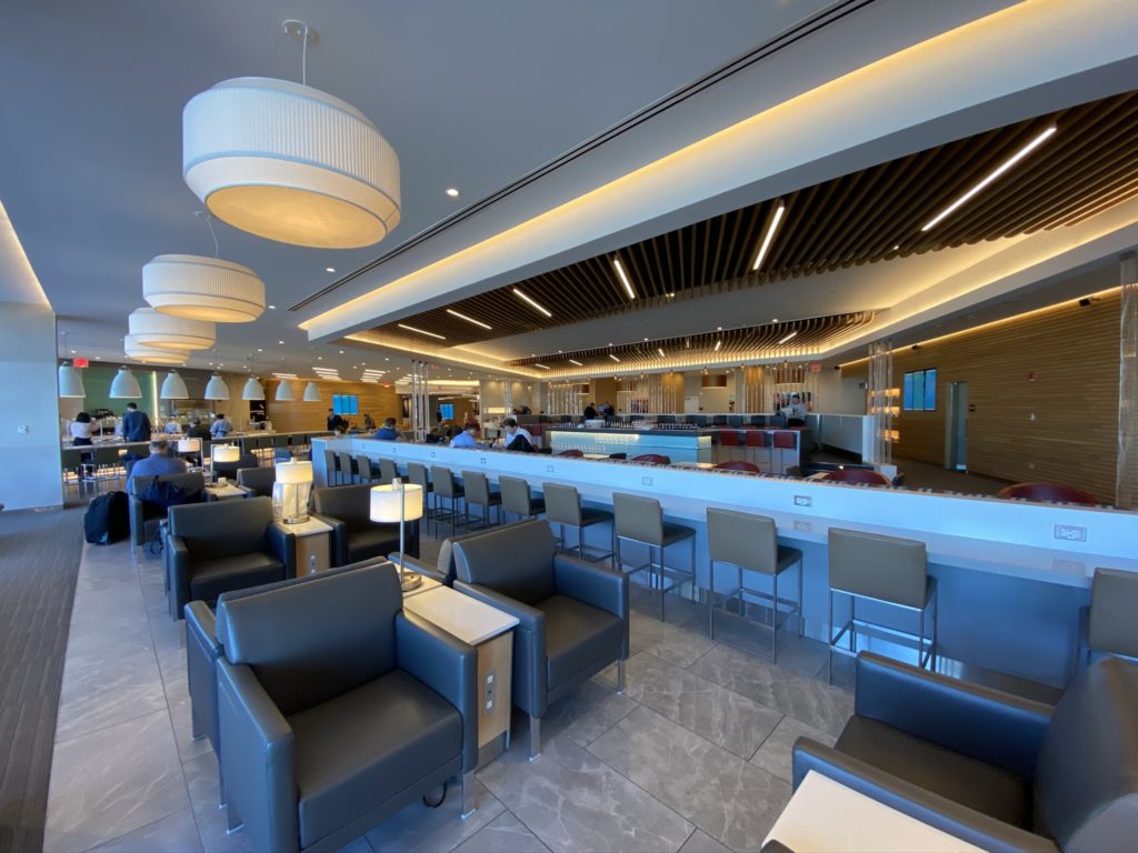 American Flagship Lounge with multplie seating options in grey leather and large white bowl like hanging lights