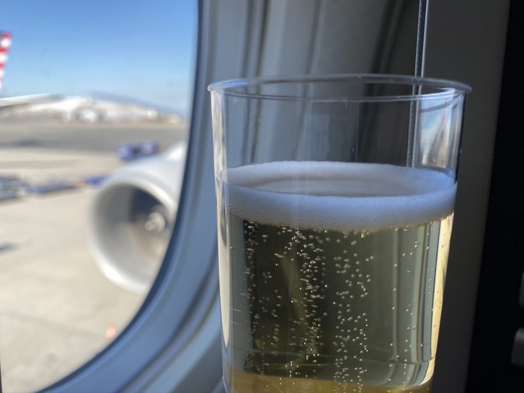 a glass of sparkling wine being held up in front of the aircraft windown which look out onto the engine