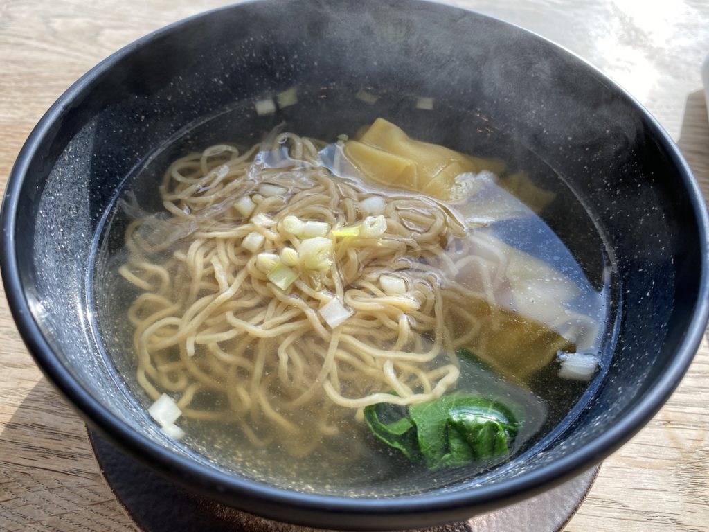 A black bowl filled with a broth soup with noodles