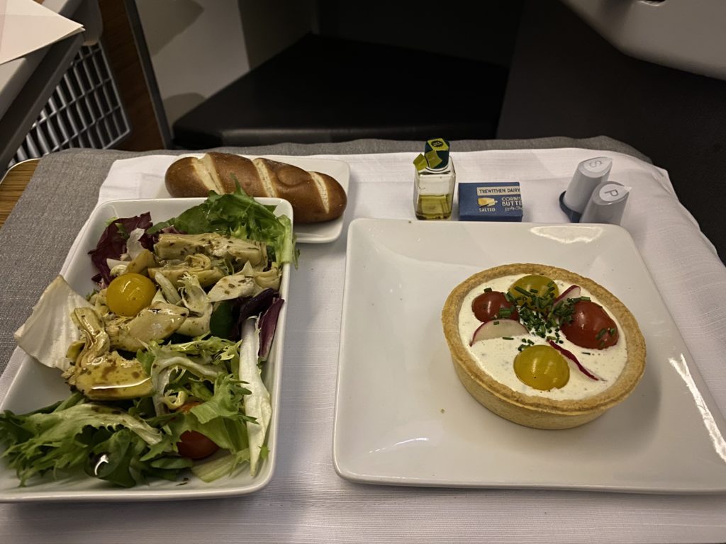 A side salad, role and a tomato tart appetizer on an aircraft tray table