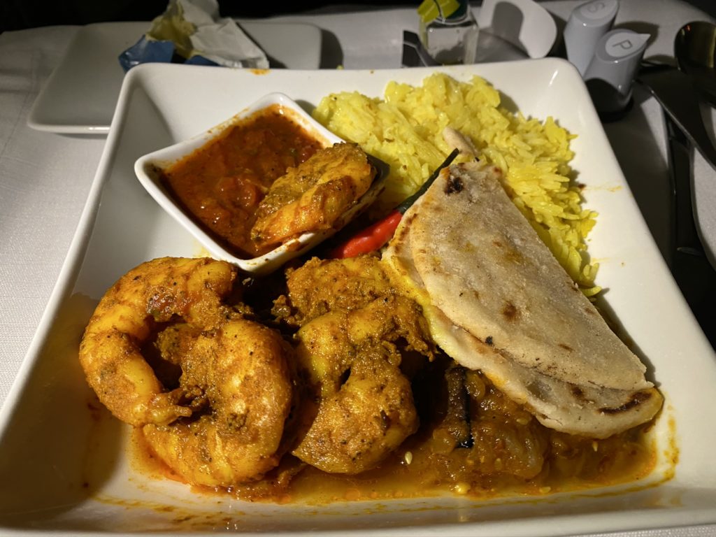 An Indian-themed inflight meal with shrimp, rice, a lot of sauce and naan bread