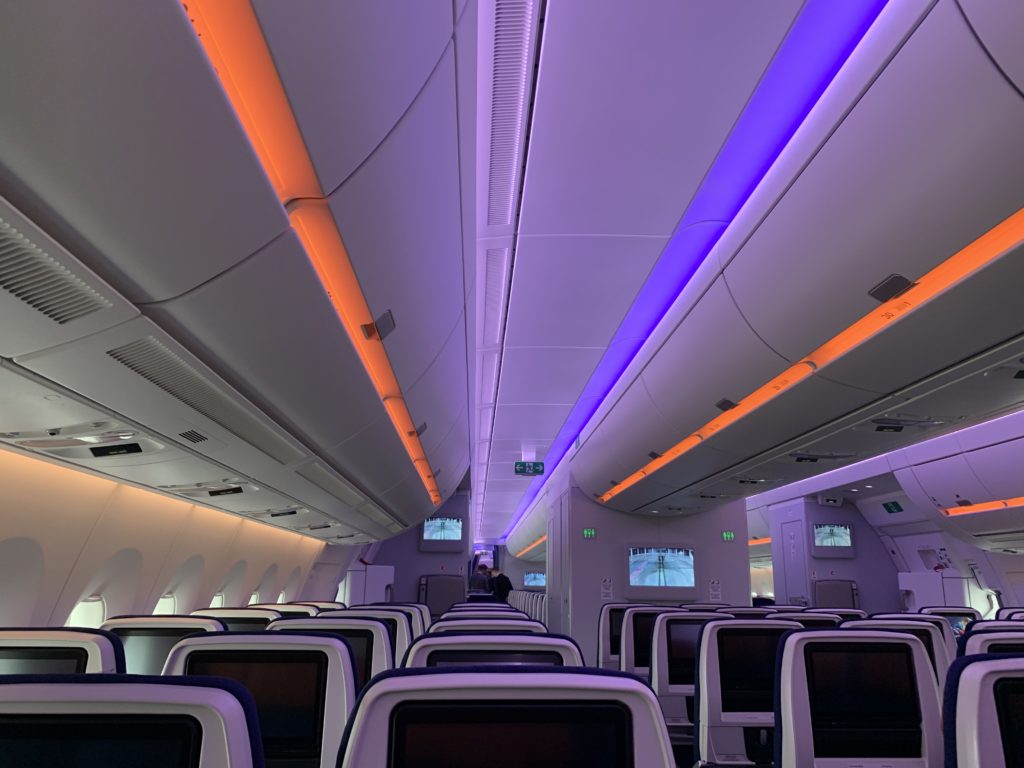 Purple and orange LED lights on the ceiling and overhead bins, seen above rows of economy class seats with seatback IFE