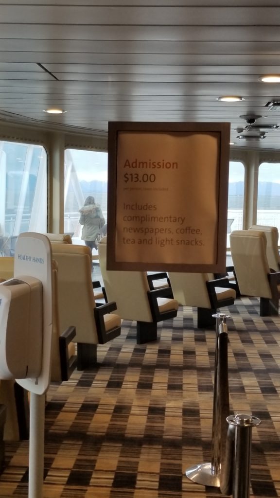 A sign stating that the lounge costs CAD$13 to enter. Comfortable cream chairs are in the background, and a plush carpe.