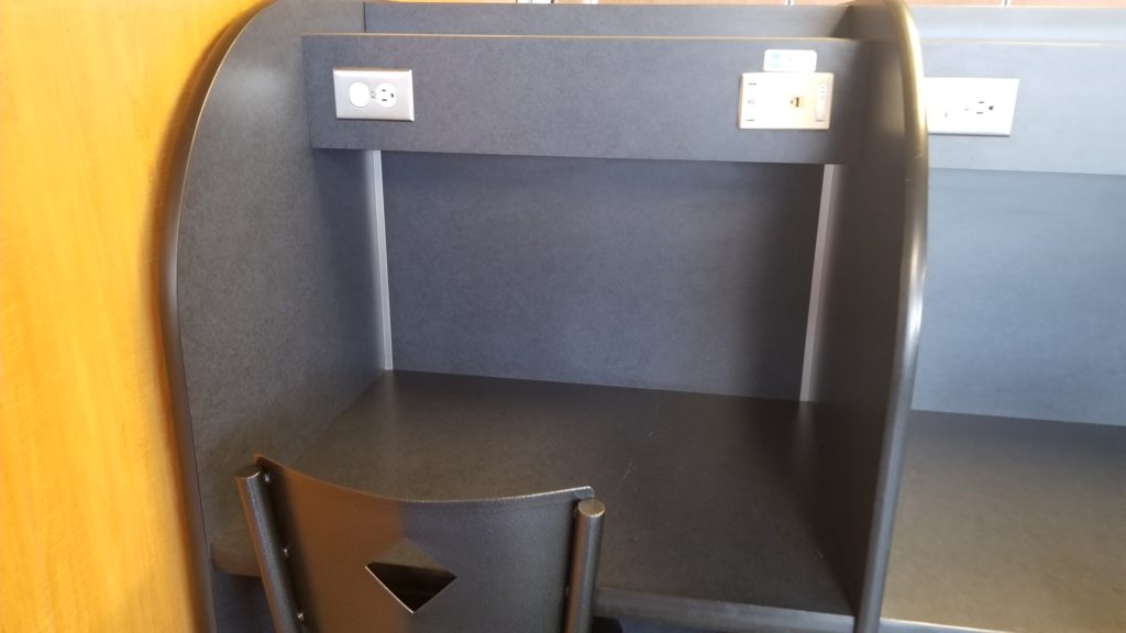 A cubicle with a desk, chair and power ports