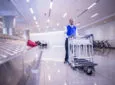 A man wheels sparkling clean luggage carts beside the baggage claim area in an airport