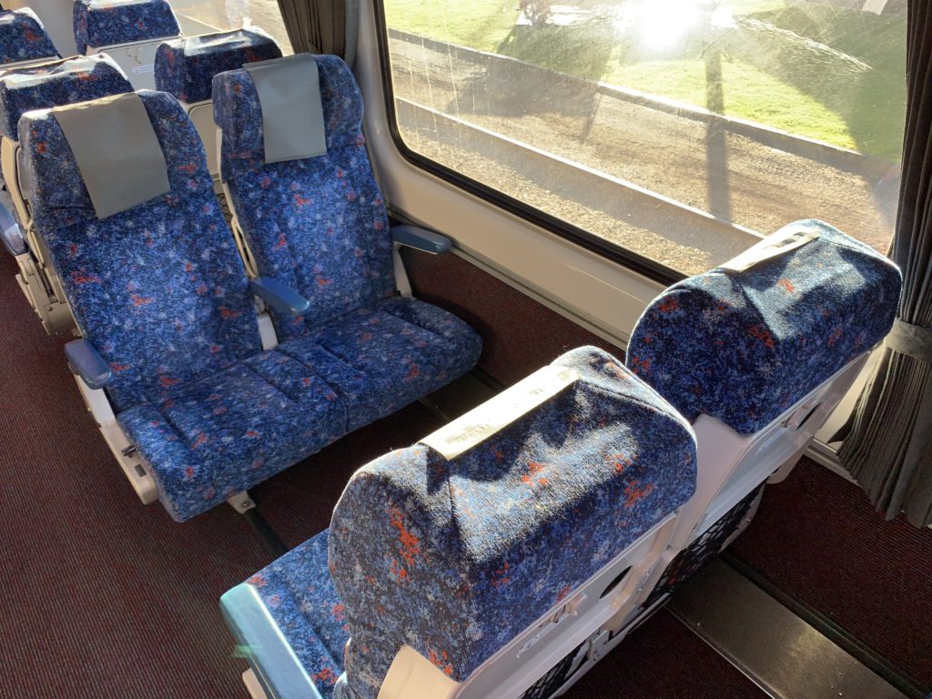 A seat quad on the train, with blue material. Two seats are facing another two seats