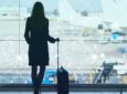 A woman stands with her suitcase in front of a large glass window at an airport