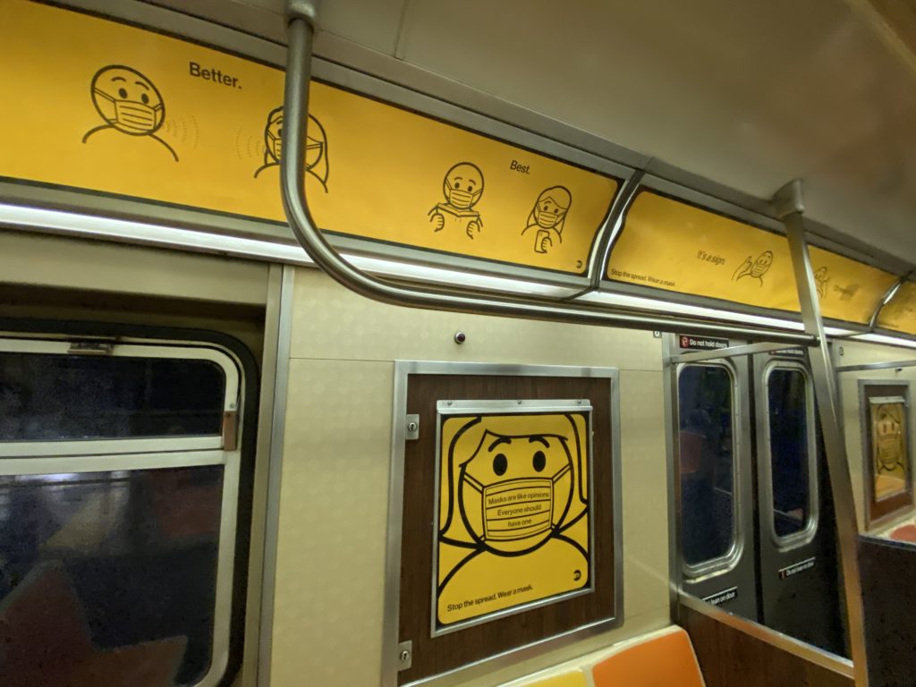 Inside a subway car. Yellow signage shows passengers how to correctly wear a mask.