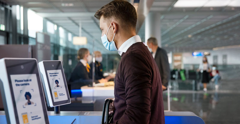 Man wearing a mask standing at the biometrics kiosk