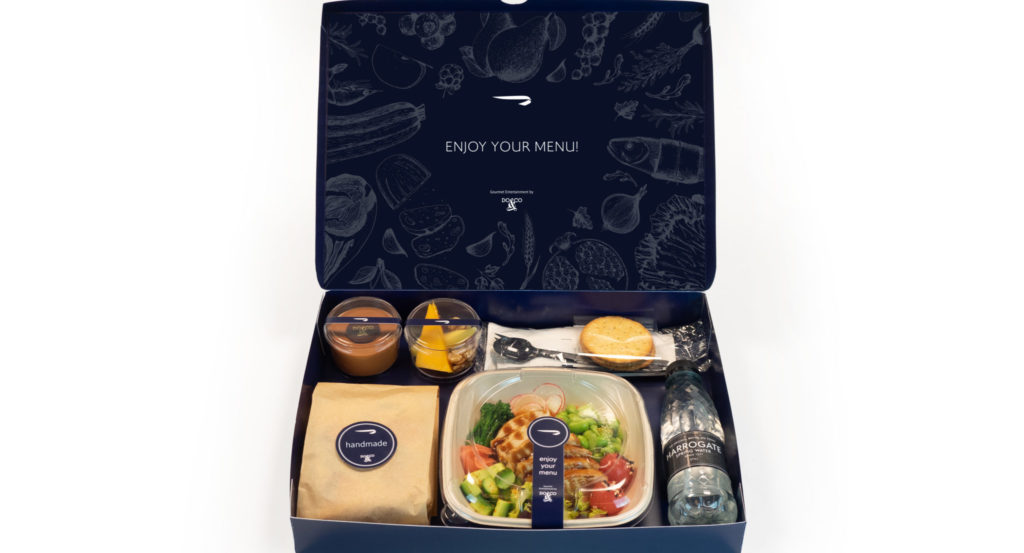 A box containing various plastic-wrapped or enclosed dishes including a salad and sides, plus a bottle of water.