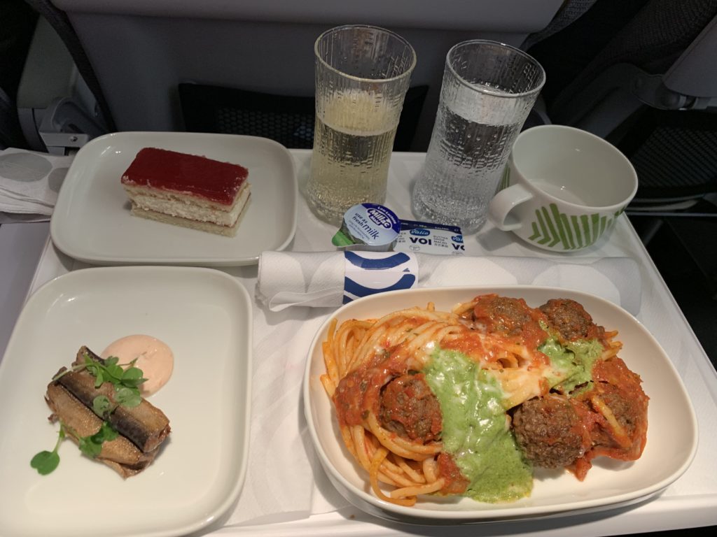 An aircraft tray table with a main course of pasta, a side dish and a dessert with champagne and water. 