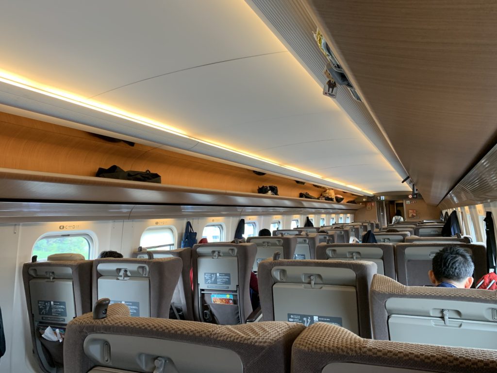 Seats configured in a 2-2 layout in business class, with beige material on the seats and orange-colored overhead bin space