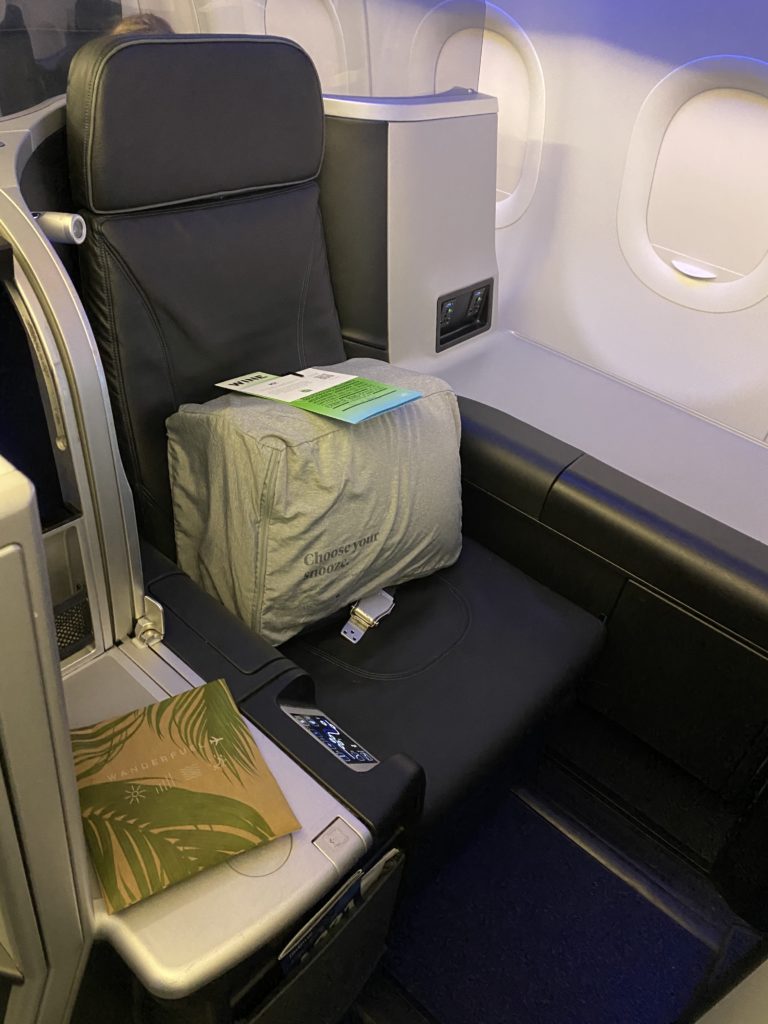 A bag of fresh bedding sits atop the Mint business class seat.