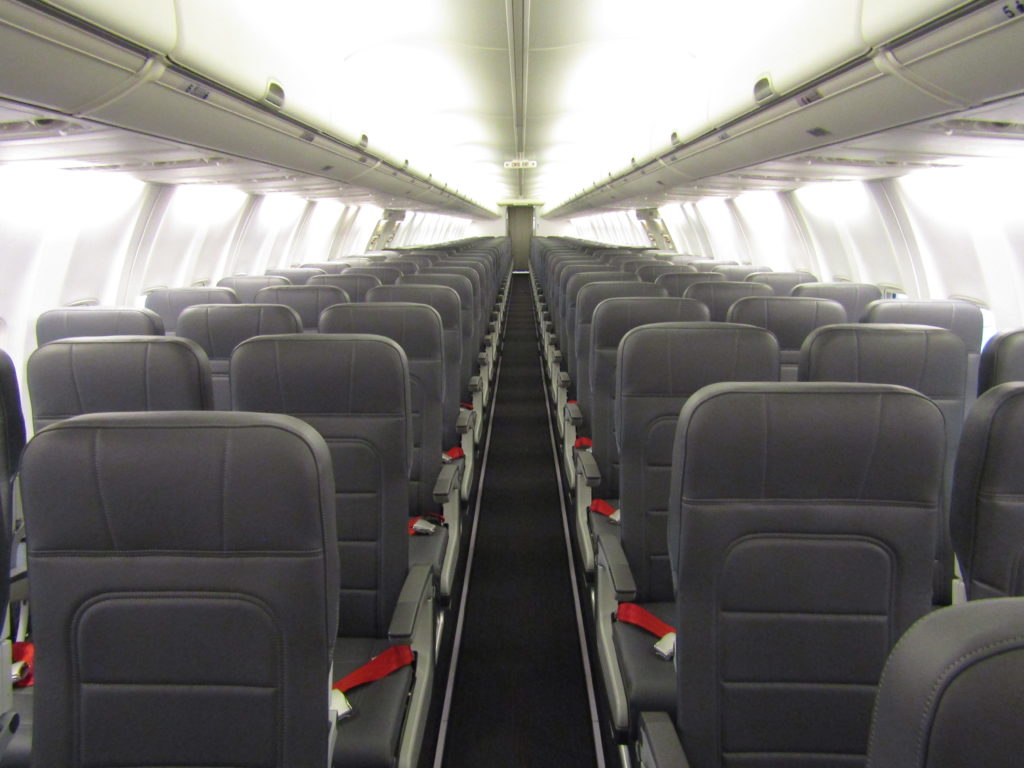 Rows of TSI seats aboard a 737-800 operated by AnadoluJet. The seats are dark grey and feature red seat belts.