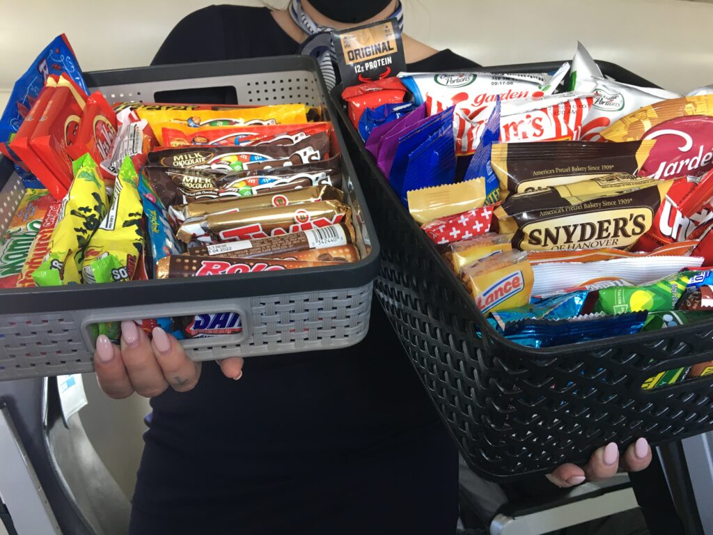 Aircraft crew holding a variety of snacks in two baskets.