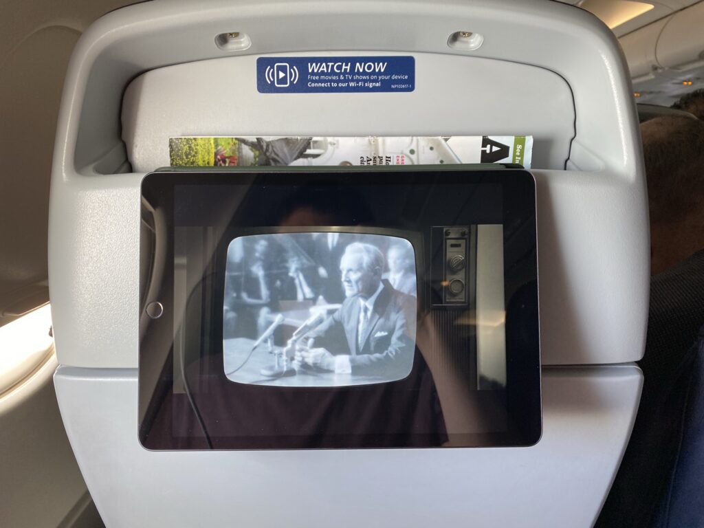 Ipad being held up on an aircraft seatback in the literature pocket.