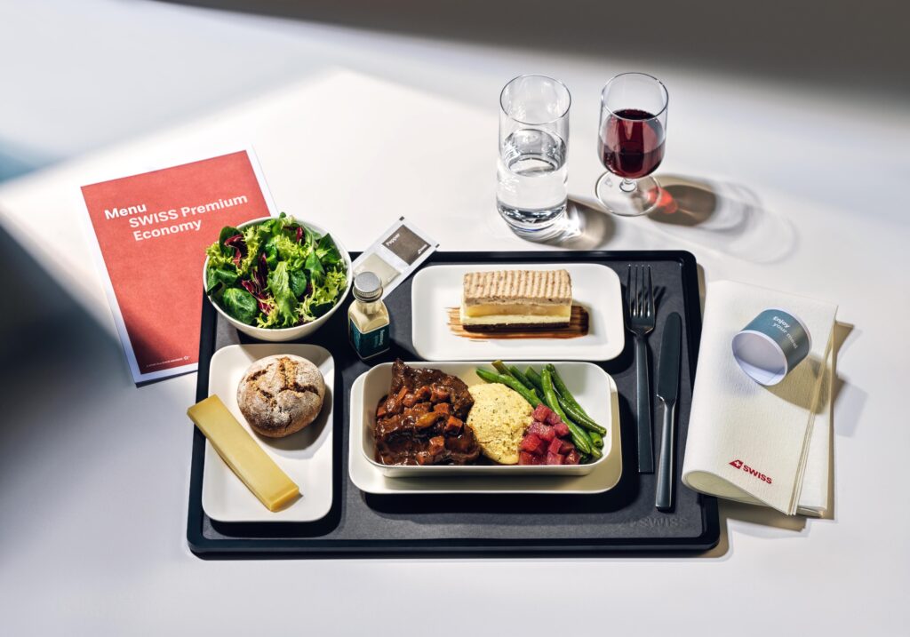 SWISS Premium Economy Class meal on a tray displayed with a menu and two glasses. One with wine and one with water.