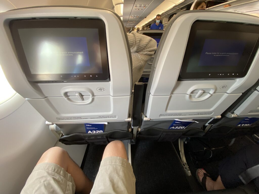 JetBlue A320 interior. This is a view of the back of the seat also showing a man's knees. He has plenty of legroom