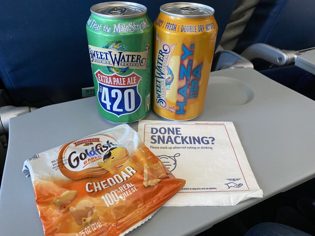 Goldfish crackers snack and two cans of beer on the tray table aboard the 757-200