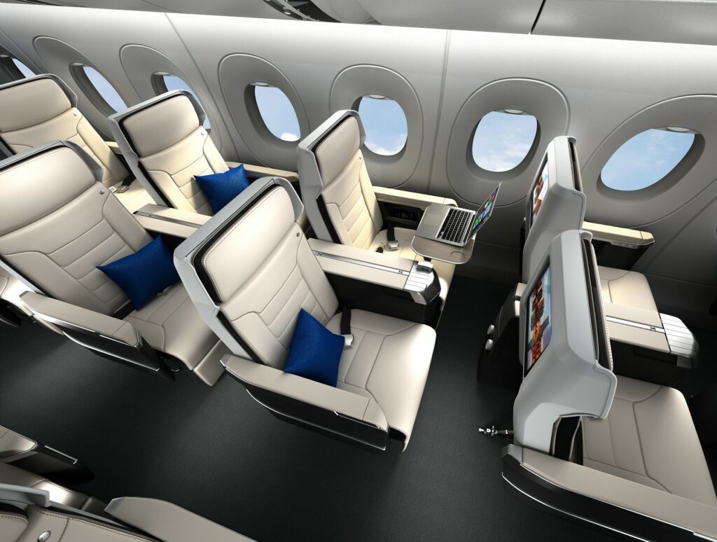 Safran Seats Z600 rendering in an aircraft. All white seats with black trim. Blue pillows on each seat and one seat has a laptop displayed on a tray table