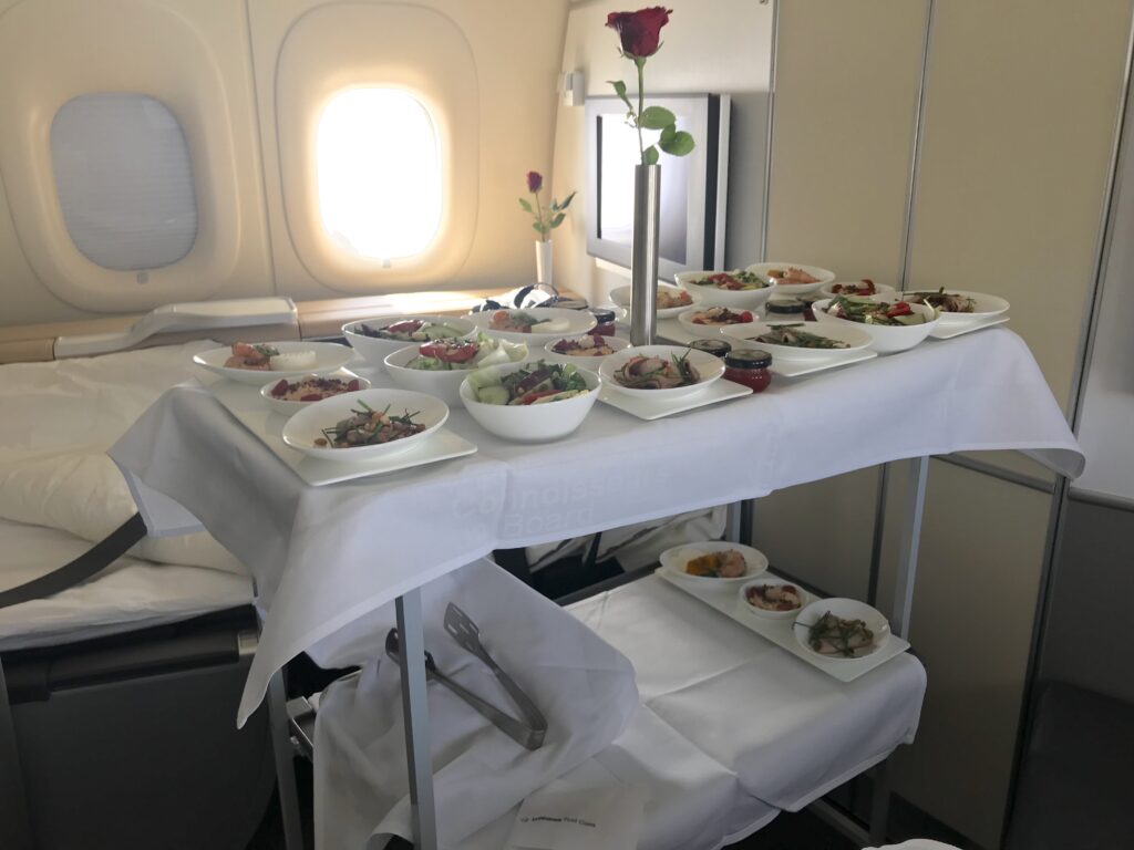 Aircraft trolley with a display of a first course meal in first class. A white cloth covers the two-tiered trolley