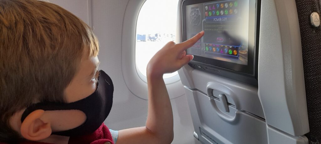 The author's child, wearing a black mask, uses the seatback IFE onboard an Aer Lingus A321neo