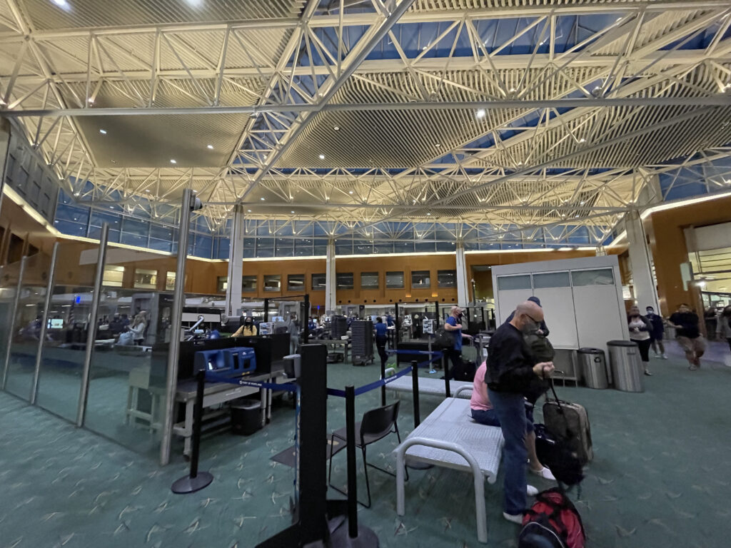 Portland Airport Security in a large temporary open space. Masked passengers are seen in different areas. 