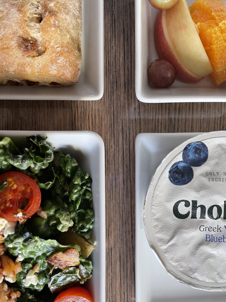 Alaska Airlines meal on a tray table. Breakfast of salad, yogourt, fruit and a pastry.