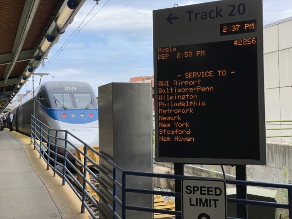 Amtrak sign in front of a parked train. The sign indicates the many stops of the trains route.