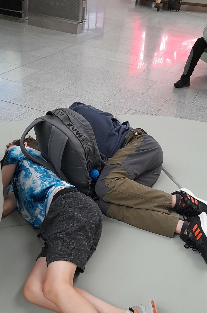 Two children laying on the floor of the airport due to delays during a transatlantic flight.