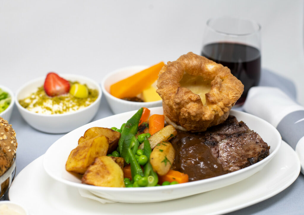 British Airways Roast Beef dinner being displayed with a glass of red wing and a fruit dessert.