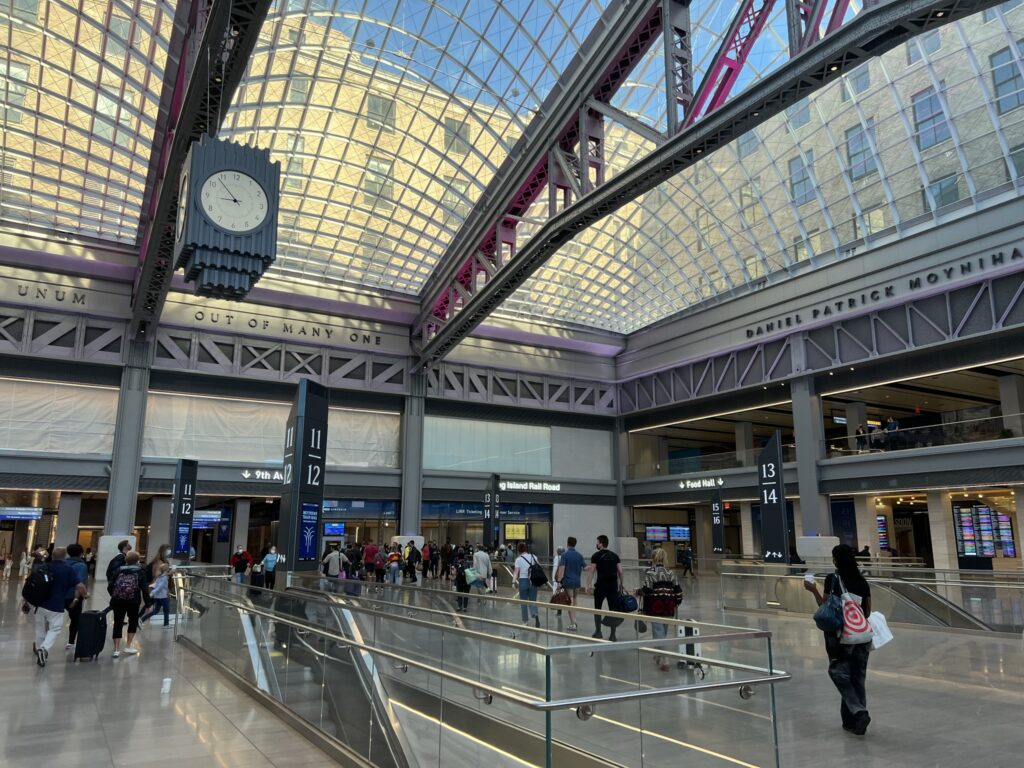 Inside the Moynihan Train Hall with large windowed ceilings and people scattered about.