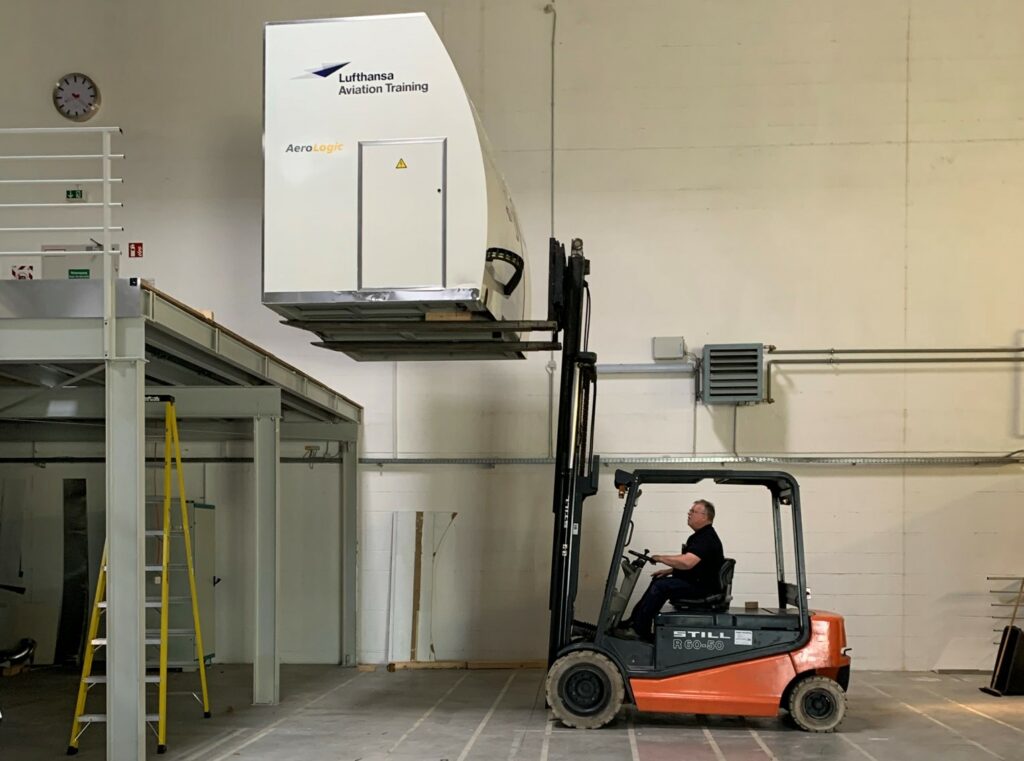 A forklift is carrying an aircraft cabin simulator.