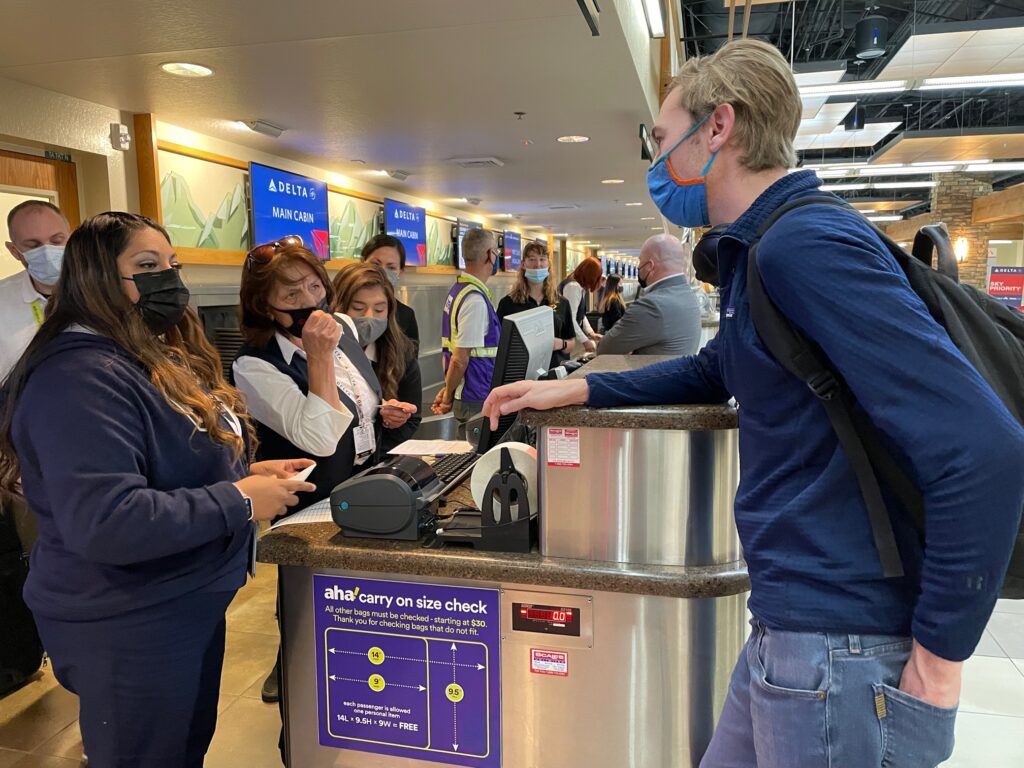 aha! check-in counter with multiple agents in masks, and a passenger being checked in