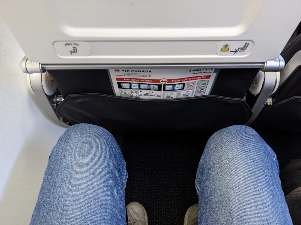 A man's knees are visible while sitting in an Air Canada Boeing 737 MAX 8 economy class seat