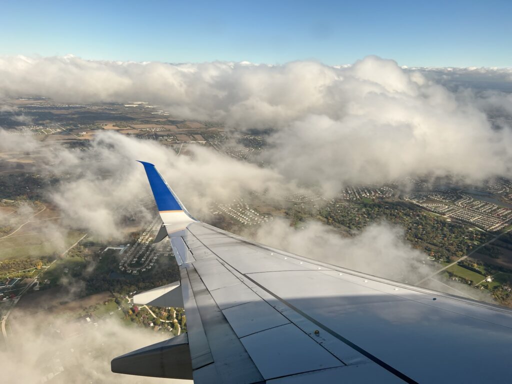 United wing tip, as the aircraft flies over a residential area with lots of green space.