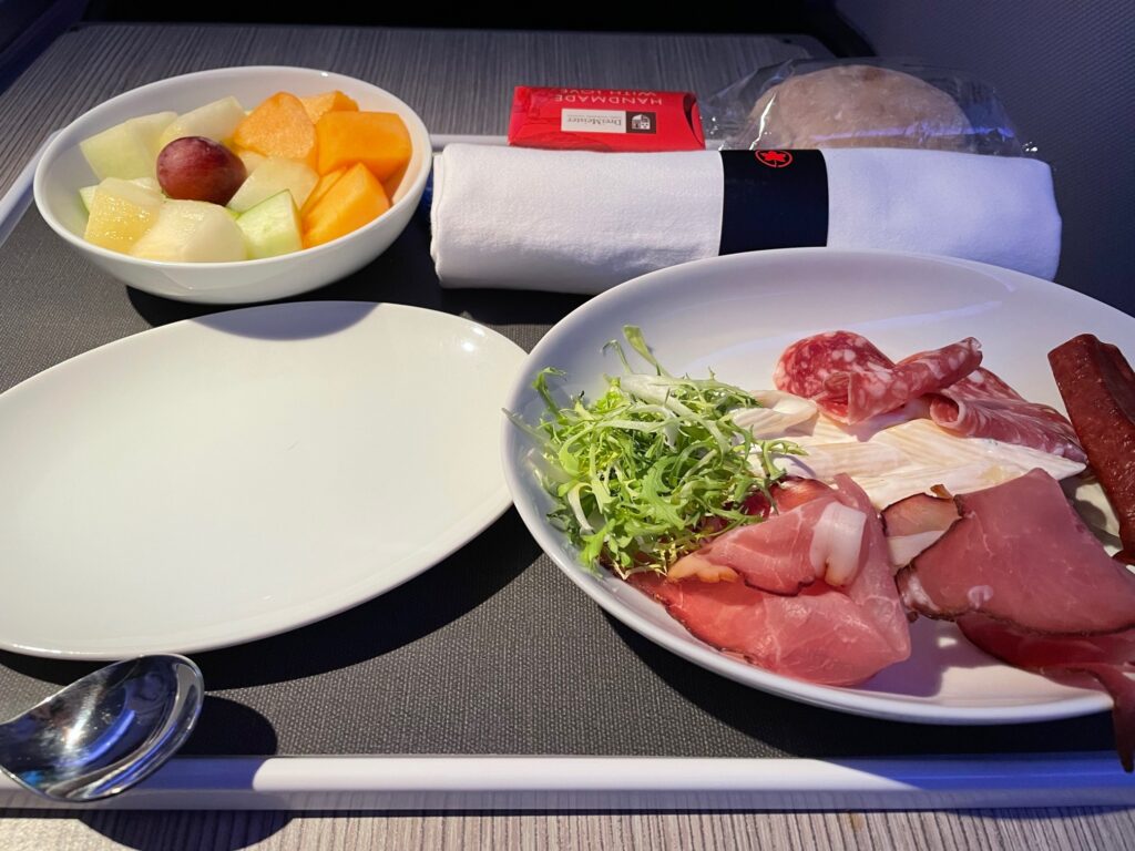 Meat and cheese on a plate, with a side dish of fruit, on the tray table