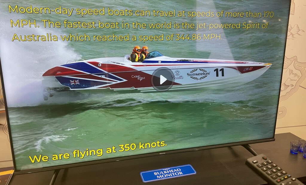 A television displaying a video that is part of the Goji Entertainment system. The view is od a speed boat in red, white and blue. 