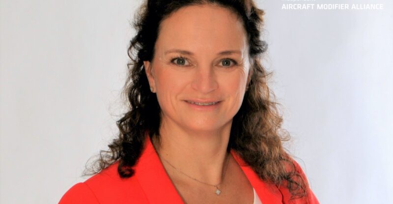 Nina Schulz managing director of IAMA poses in an orange jacket and white shirt.